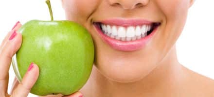 Woman holds apple next to her healthy smile