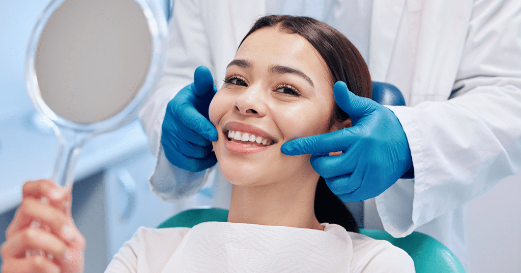 Woman smiling in dentist's chair holding a mirror.