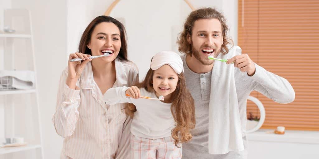 Little Girl And Her Parents Brushing Teeth In Bathroom