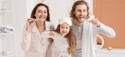 Little Girl And Her Parents Brushing Teeth In Bathroom