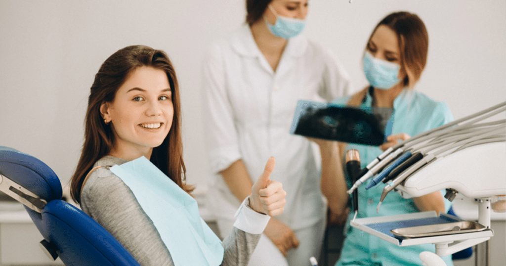 Dental patient giving a thumbs up with two dentists standing in the background.