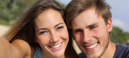 Couple outside with beautiful teeth smiling after getting cosmetic procedures from a holistic dentist