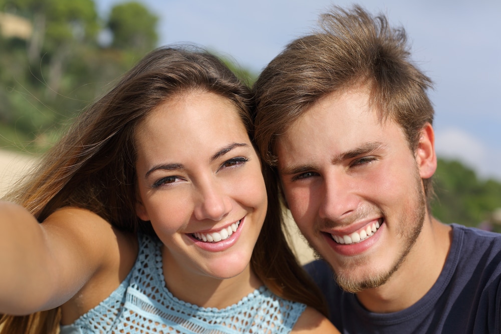 Couple outside with beautiful teeth smiling after getting cosmetic procedures from a holistic dentist